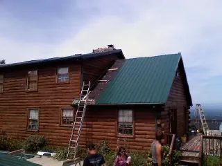 Green metal roof going on a two story log home with ladders set in Shiloh